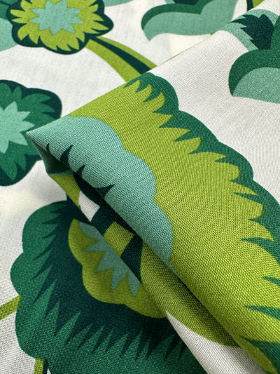 Close-up of Designer Rayon - Verdant Bloom (145cm) by Super Cheap Fabrics, showcasing green and blue floral prints on white rayon. The slightly folded fabric highlights its versatile use for various projects.