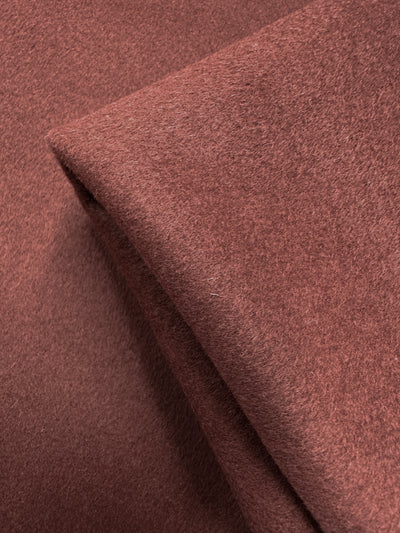 Close-up of Super Cheap Fabrics' Wool Cashmere - Fired Brick (154cm), showing two overlapping folded pieces and highlighting the luxurious, soft, felt-like texture of its reddish-brown fabric.