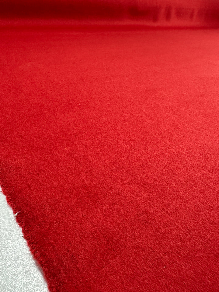 A close-up of Super Cheap Fabrics' Wool Cashmere - Lava Falls - 150cm shows its luxurious, soft, slightly fuzzy red surface spread flat, with fabric edges visible in the lower left corner.