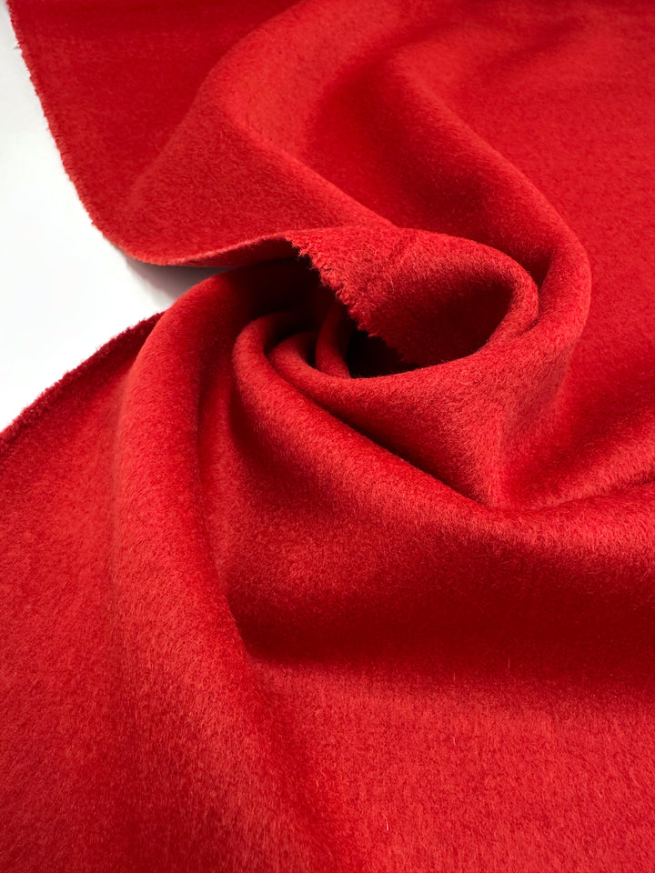 Super Cheap Fabrics’ Wool Cashmere - Lava Falls - 150cm is a bright red, heavy weight wool blend with a soft, plush surface and gentle folds, shown loosely twisted to highlight its smooth texture against a white background.