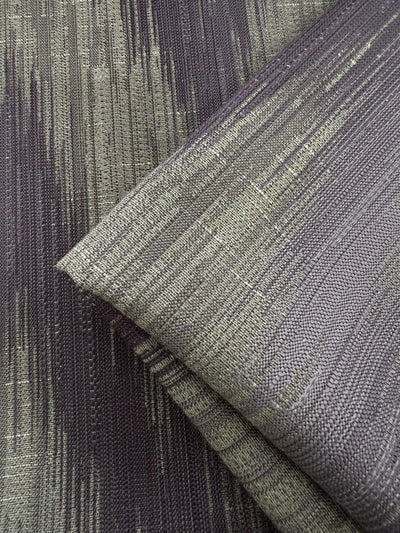 A close-up image of Upholstery Jacquard - Dusk - 145cm with a modern, abstract pattern. The fabric has a vertical streak design in shades of grey and light gold, creating a textured and dynamic appearance. Part of our affordable range from Super Cheap Fabrics, this durable stylish fabric is perfect for any interior project.