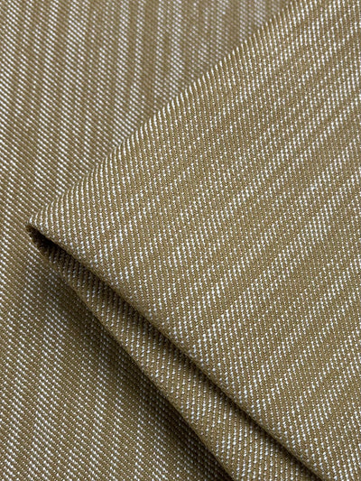 Close-up of beige and gray striped fabric, neatly folded at one corner. The stripes, set in a twill weave, form a subtle diagonal pattern, creating a textured and visually appealing design. This durable fabric appears to be of medium weight and has a smooth finish. The product is Upholstery Twill - Caramel - 147cm from Super Cheap Fabrics.