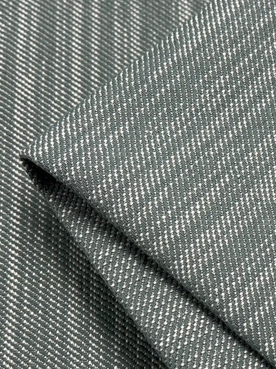 Close-up of a folded piece of fabric with a fine, diagonal striped pattern in shades of gray and white. The smooth and soft texture flaunts a twill weave, creating a subtle linear design ideal for durable upholstery. This is the Upholstery Twill - Sea Mist - 147cm from Super Cheap Fabrics.
