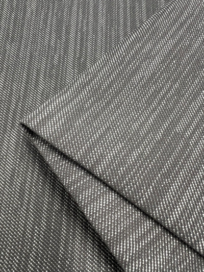 Close-up image of a piece of gray fabric with a subtle woven pattern, featuring small white diagonal lines. The Upholstery Twill - Dove Grey - 147cm by Super Cheap Fabrics is slightly folded at the corner, showcasing its texture and design, ideal for furniture upholstery.