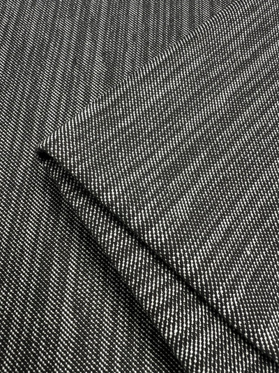 A close-up image of folded black and white pinstripe fabric, perfect for furniture upholstery. The durable fabric, Super Cheap Fabrics Upholstery Twill - Salt & Pepper - 147cm, has a diagonal pattern created by thin, evenly spaced white lines on a black background. The fold creates an angled intersection of the lines, adding depth and texture to the image.