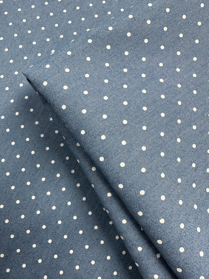 Close-up of Chambray - Blissful Spot (150cm) by Super Cheap Fabrics, featuring lightweight blue chambray with a white polka dot pattern and a folded section at the center.
