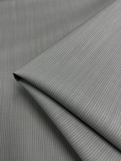 A close-up shot of neatly folded, medium weight pinstripe fabric. The Merino Wool Suiting - Gray & White Stripe - 155cm by Super Cheap Fabrics boasts thin light-gray vertical stripes evenly spaced against a darker gray background, showcasing its smooth texture and fine details.