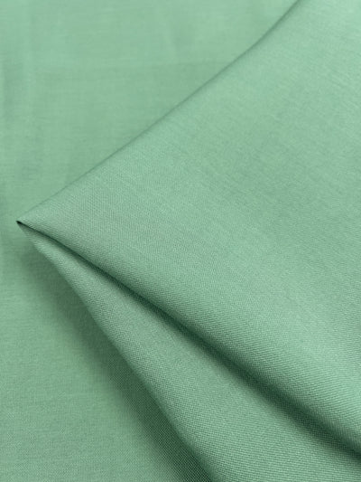 A piece of Super Cheap Fabrics Bamboo Suiting - Hemlock - 140cm is folded, showing a smooth texture and subtle sheen. The lightweight fabric has a uniform color and appears to be exceptionally soft.