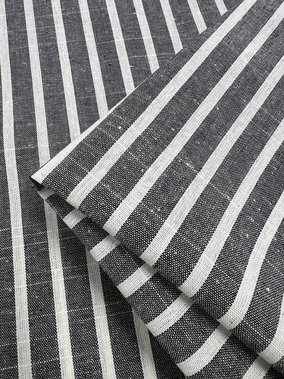 Close-up image of a folded Linen Cotton - Dark Grey Stripe fabric from Super Cheap Fabrics. The pattern features evenly spaced vertical white stripes on a dark grey background, creating a classic, textured look. This natural fiber fabric appears to be neatly arranged, highlighting its durable design clearly.