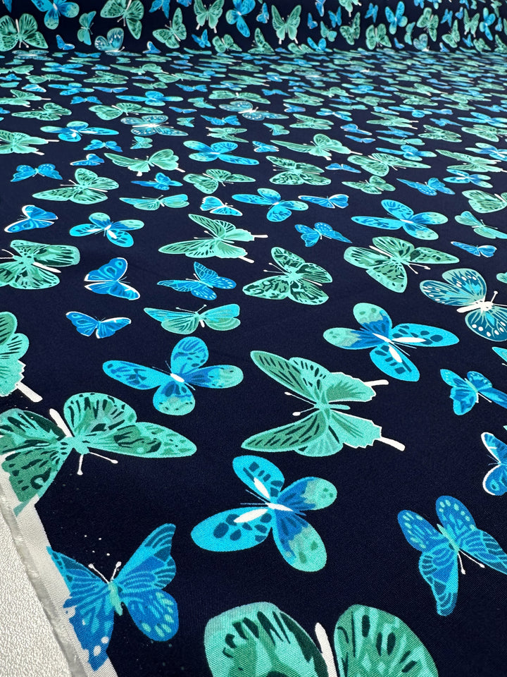 Super Cheap Fabrics' Designer Rayon - Midnight Flutter (145cm) features vibrant blue and teal butterflies on a dark navy background, creating a lively and versatile fabric for any project.