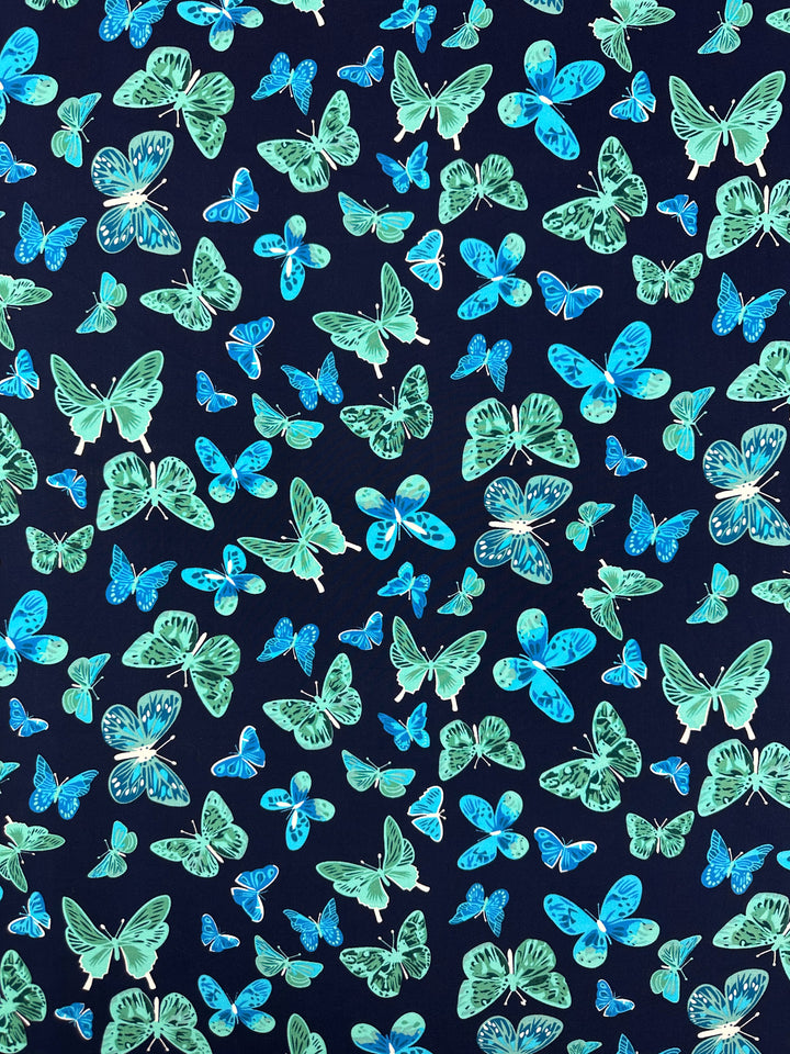 The Designer Rayon - Midnight Flutter by Super Cheap Fabrics features green and blue butterflies on a dark navy background, offering vibrant and versatile prints across a 145cm wide fabric.