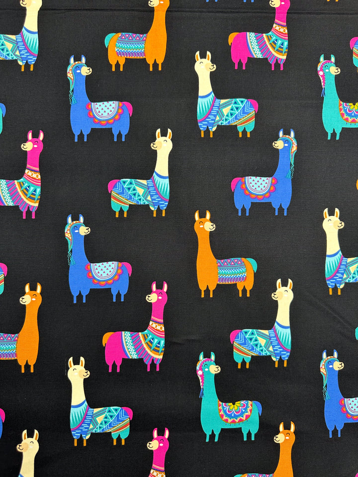 The Cotton Duck - Lama Lama - 120cm by Super Cheap Fabrics features a stylish pattern of colorful llamas set against a black backdrop, ideal for trendy home décor. The llamas are depicted in various poses, draped in vibrant multicolored cotton blankets and accessories, contributing to a lively and whimsical design.