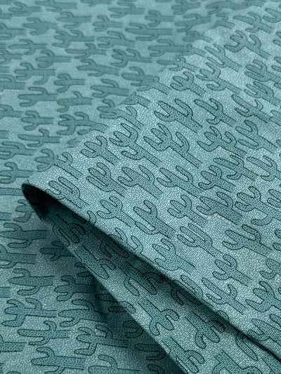 The Cotton Duck - Teal Texas - 120cm by Super Cheap Fabrics showcases a pattern of dark blue cacti printed on the fabric. Ideal for home décor, the folded layers consistently display a cactus design that brings a stylish flair to any project.