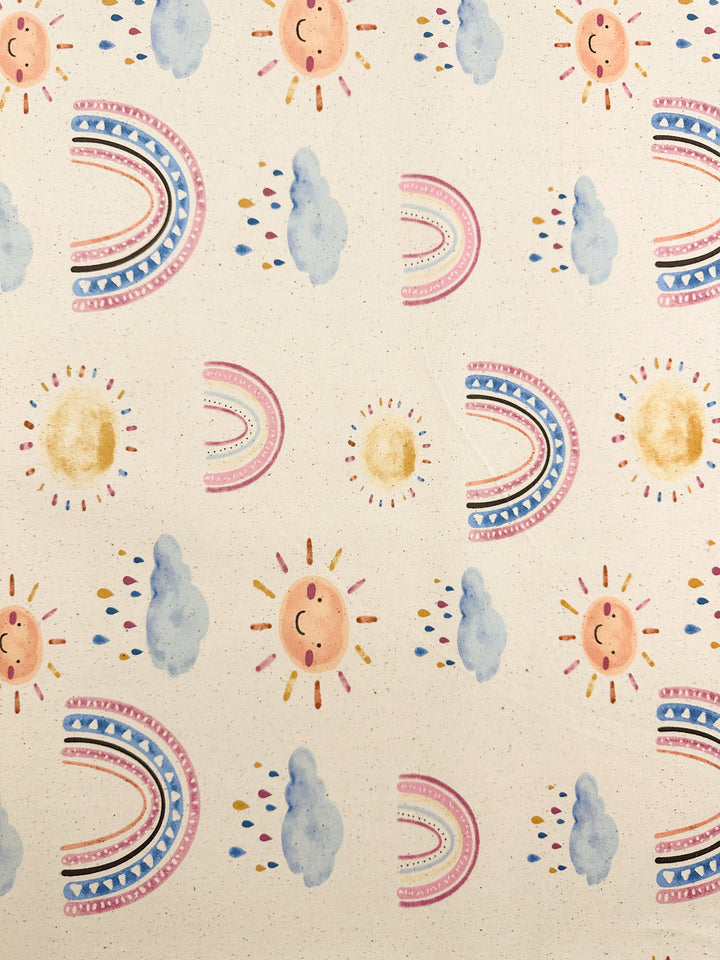 The Cotton Duck - Rainbow Natural - 112cm by Super Cheap Fabrics showcases a patterned illustration on medium weight cotton fabric, adorned with smiling suns, clouds, and rainbows against a beige background. The pastel hues and radiant suns contribute to a cheerful and whimsical home décor aesthetic.