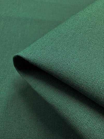 A close-up view of the folded Ramie Linen from Super Cheap Fabrics showcases a textured weave crafted from natural fiber. The Hunter Green fabric appears smooth and soft, draping gracefully to form a visible fold, with its color reflecting the deep, rich green reminiscent of organic elegance.