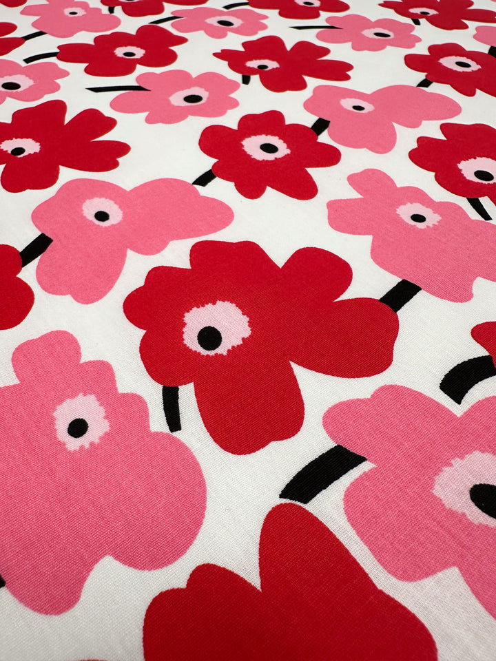 Introducing the eye-catching Printed Cotton - Little Miss Sunshine by Super Cheap Fabrics. This fabric features a vibrant floral design with red and pink poppies, complete with black centers, set against a crisp white background. Made from natural cotton fibers, it's perfect for various applications. Measuring 150cm wide, it offers versatility and quality for all your creative projects.