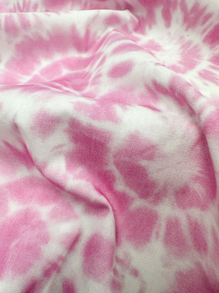 A close-up of the Super Cheap Fabrics Printed Cotton in Rosebloom - 150cm reveals the gentle texture of natural cotton fibers, with its soft fabric displaying a pink and white tie-dye pattern. The crumpled material showcases various shades of pink blending seamlessly with the white.