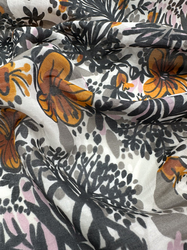 A detailed view of the Printed Silk Voile - Garzen by Super Cheap Fabrics, showcasing its extra lightweight composition with a floral design featuring orange flowers and dark leaves on a white backdrop. The fabric is elegantly draped to reveal soft folds and shadows, making it ideal for creating stylish clothing accessories.