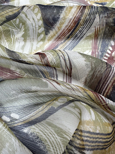 A detailed look at the Pure Printed Silk - Feathers by Super Cheap Fabrics, showcasing an abstract pattern with wavy, multicolored lines and shapes in shades of green, brown, yellow, and black. Its extra-lightweight quality gives it a textured and dynamic appearance ideal for crafting elegant dresses.