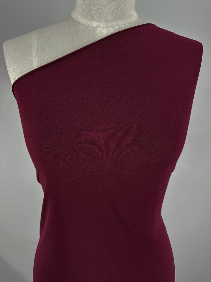 A mannequin showcases the ITY Knit - Merlot, a one-shoulder garment crafted from medium weight polyester spandex fabric by Super Cheap Fabrics, elegantly set against a plain background.