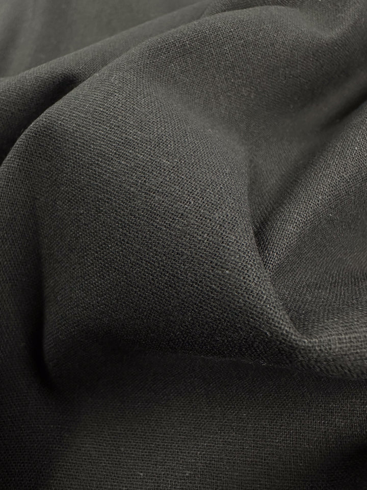 A close-up of the Super Cheap Fabrics' Ramie Linen in black, 150cm wide, showcasing its natural fiber composition and textured weave as it drapes in soft folds.