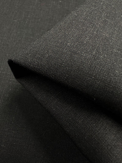 Close-up of the Linen Voile - Black - 140cm by Super Cheap Fabrics, accentuating its texture and weave. This cotton linen is meticulously folded, highlighting the smooth surface and intricate detail of the lightweight material.