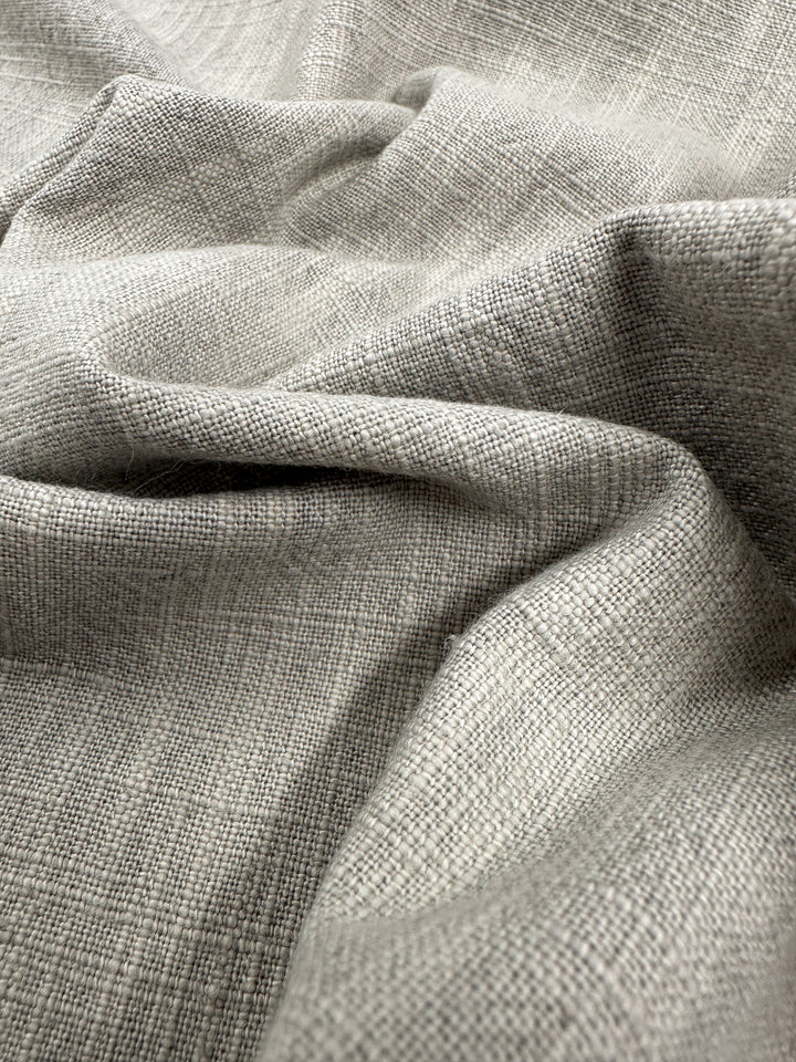 Close-up of the Basket Dyed Cotton in Dove from Super Cheap Fabrics, featuring a textured and woven pattern. The light gray upholstery fabric appears soft and slightly crumpled, highlighting its fine threads and natural folds characteristic of its twill weave.