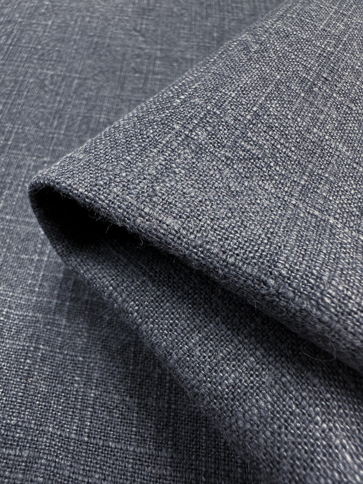 Close-up of a navy, textured upholstery fabric with a folded corner, showcasing a basket dyed pattern. The heavy weight fabric from Super Cheap Fabrics appears soft and durable, featuring a subtle grid-like design.