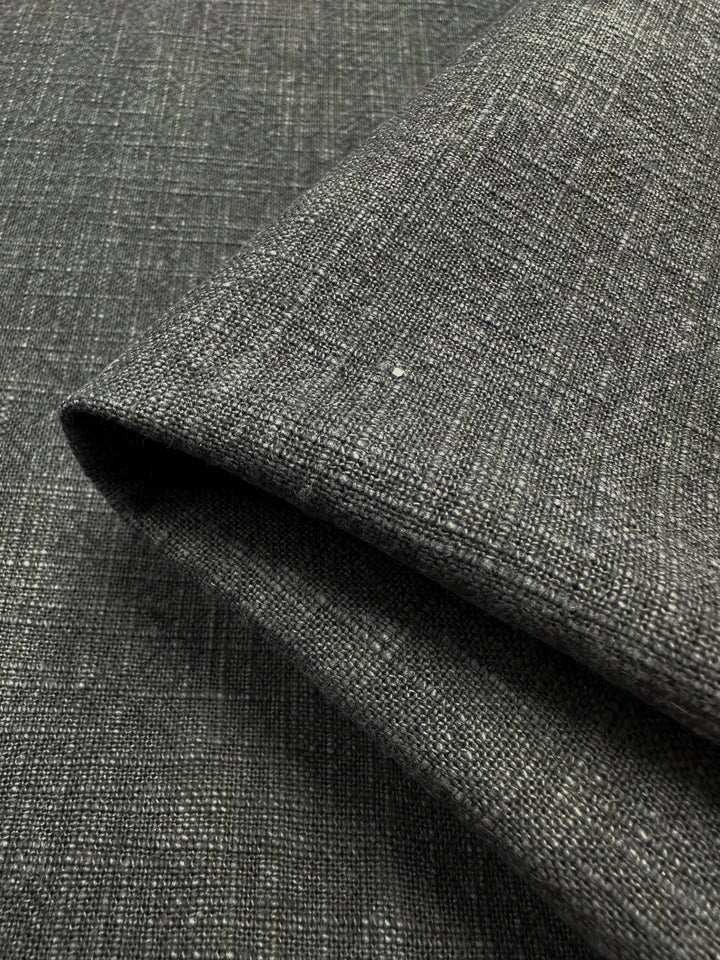 Close-up of the Basket Dyed Cotton in Charcoal from Super Cheap Fabrics, featuring 140cm wide dark gray textured upholstery fabric with a twill weave folded at the edge. The material showcases a woven pattern and subtle color variations, providing a sophisticated look.