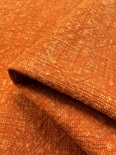 Close-up of folded Super Cheap Fabrics' Basket Dyed Cotton in Burnt Orange, featuring a textured twill weave. The 140cm-wide material is heavy yet soft, with small, subtle specks that add visual interest to the surface.