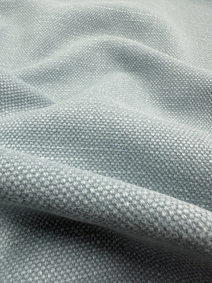 A close-up of the blue fog Canvas Linen Denim from Super Cheap Fabrics showcases its textured upholstery fabric with a woven pattern. The heavyweight material reveals gentle folds and a slightly grainy surface, adding depth and softness.