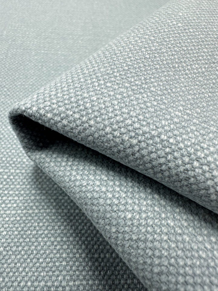 Close-up of the heavyweight fabric, "Canvas Linen Denim - Blue Fog - 140cm," by Super Cheap Fabrics. The light gray material is folded, showcasing its textured surface and detailed weave pattern with a soft, slightly matte finish reminiscent of denim canvas.