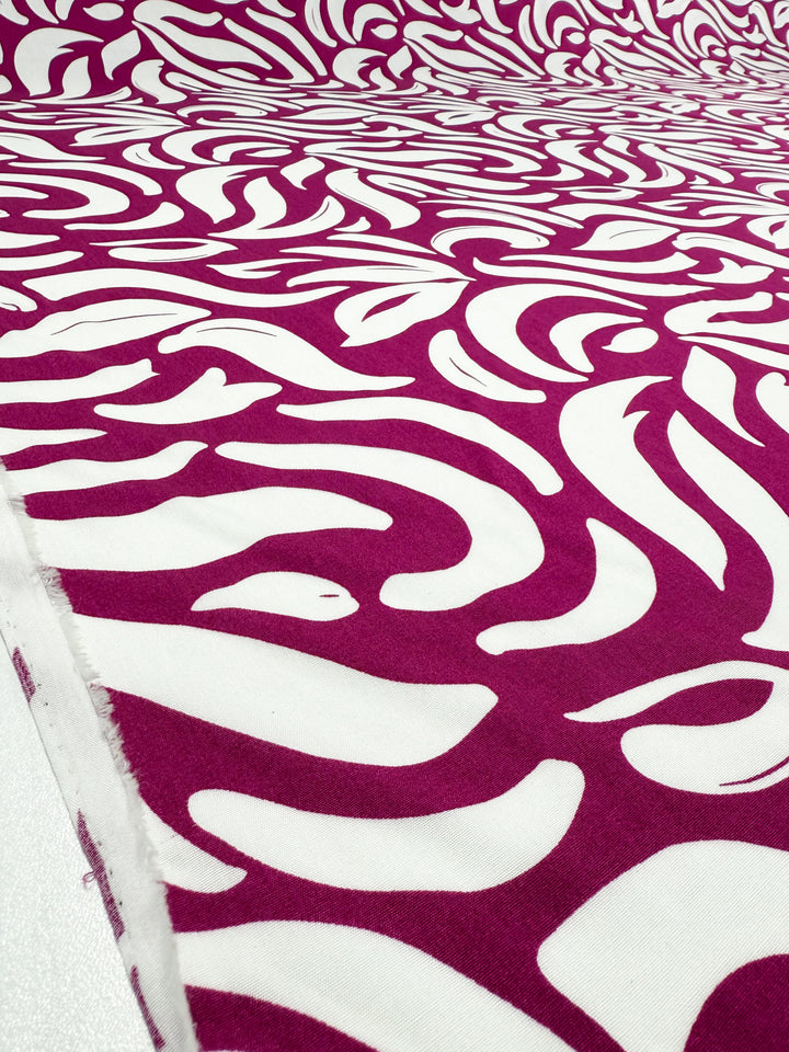 A close-up of Super Cheap Fabrics' Designer Rayon - Wild Bloom Fizz (145cm), showcasing a bold abstract white pattern on a magenta background. Ideal for those after lightweight, vibrant printed fabric.