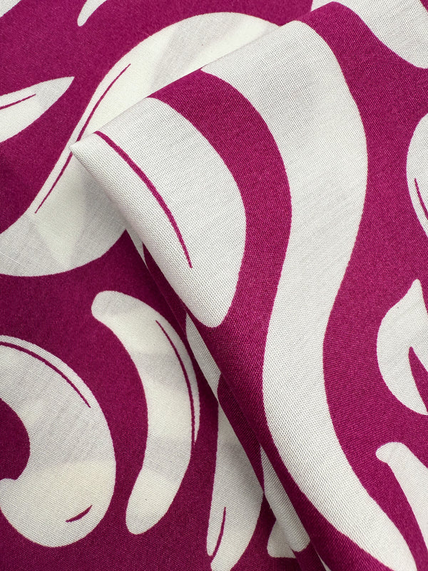 A close-up of Designer Rayon - Wild Bloom Fizz by Super Cheap Fabrics shows its smooth texture, vibrant magenta and white abstract swirl prints, and overlapping layers. Fabric width: 145cm.