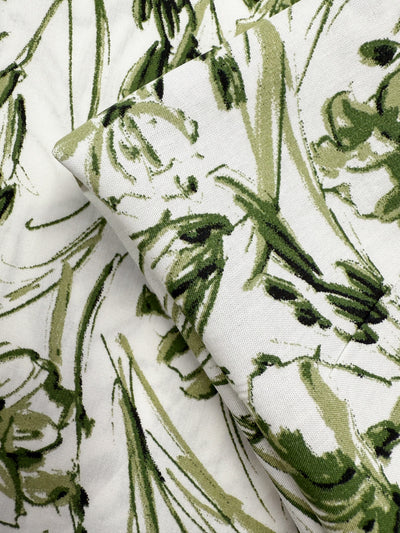 Close-up of Super Cheap Fabrics’ Designer Rayon - Olive Sketch (145cm) featuring layered white fabric with an abstract green floral pattern, showcasing its texture and brushstroke-style leaves and petals.