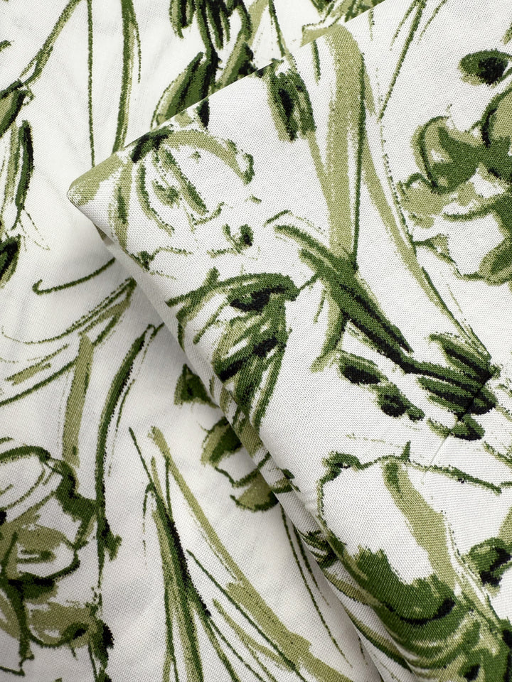 Close-up of Super Cheap Fabrics’ Designer Rayon - Olive Sketch (145cm) featuring layered white fabric with an abstract green floral pattern, showcasing its texture and brushstroke-style leaves and petals.