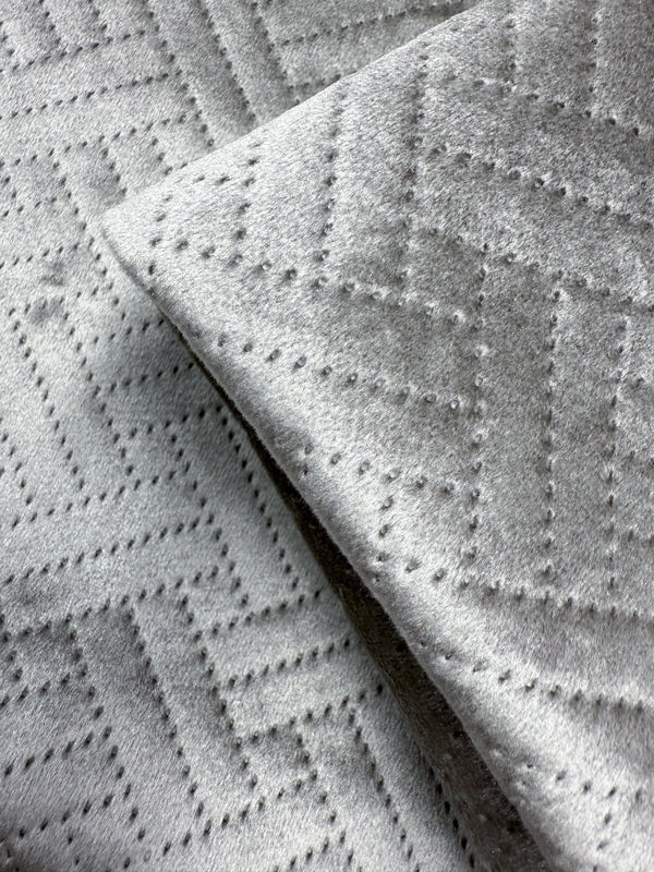 Close-up of two overlapping pieces of Embossed Velvet - Silver - 150cm by Super Cheap Fabrics, featuring soft, light grey upholstery fabric with a geometric dotted zigzag design.