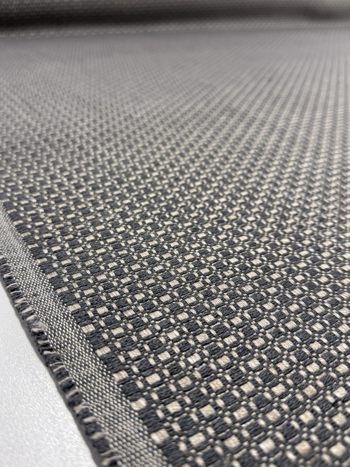 Close-up of Super Cheap Fabrics’ Upholstery Basketweave - Aria Steel (144cm): premium Australian textile with a small checkered black, gray, and off-white pattern, textured surface, and finished edge—perfect for luxury upholstery.