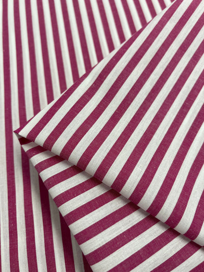 A close-up of Super Cheap Fabrics' Cotton Lawn - Lilac Rose showcases its lightweight, silky fabric featuring vertical stripes in alternating red and white colors. Made from 100% cotton and measuring 150cm wide, the fabric is arranged in multiple layers to highlight its intricate pattern and texture.