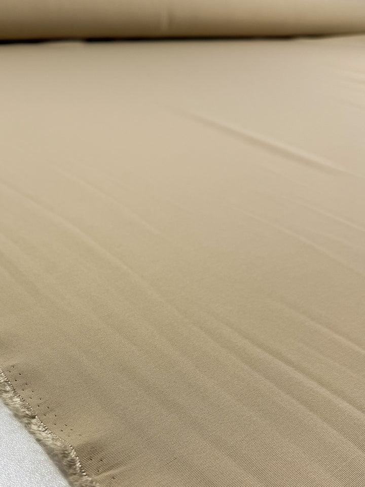 Close-up of Super Cheap Fabrics' Cotton Bengaline - Sand Drift (150cm), showcasing its smooth, beige medium-weight texture and subtle weave with a slightly unfinished edge.