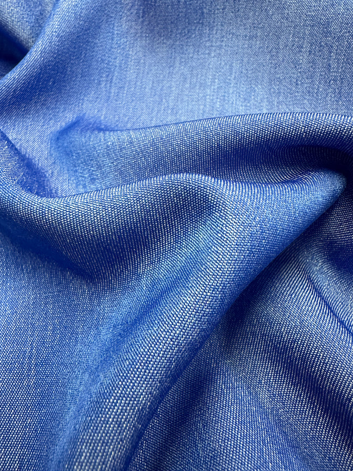 A close-up of the Chambray - Victoria Blue - 150cm fabric by Super Cheap Fabrics showcases its textured weave and flowing folds. The material exhibits a subtle sheen, highlighting the intricate pattern and depth of its surface.