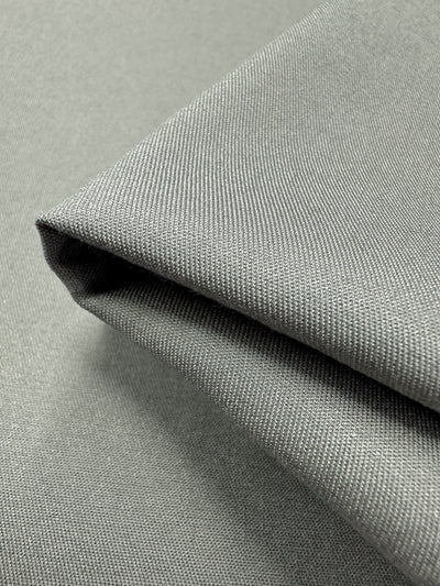 Close-up of a piece of Chambray - Flint Grey fabric by Super Cheap Fabrics, folded to showcase its textured, woven pattern. The fabric appears smooth and neatly arranged, highlighting its fine threading and a subtle sheen under the lighting.