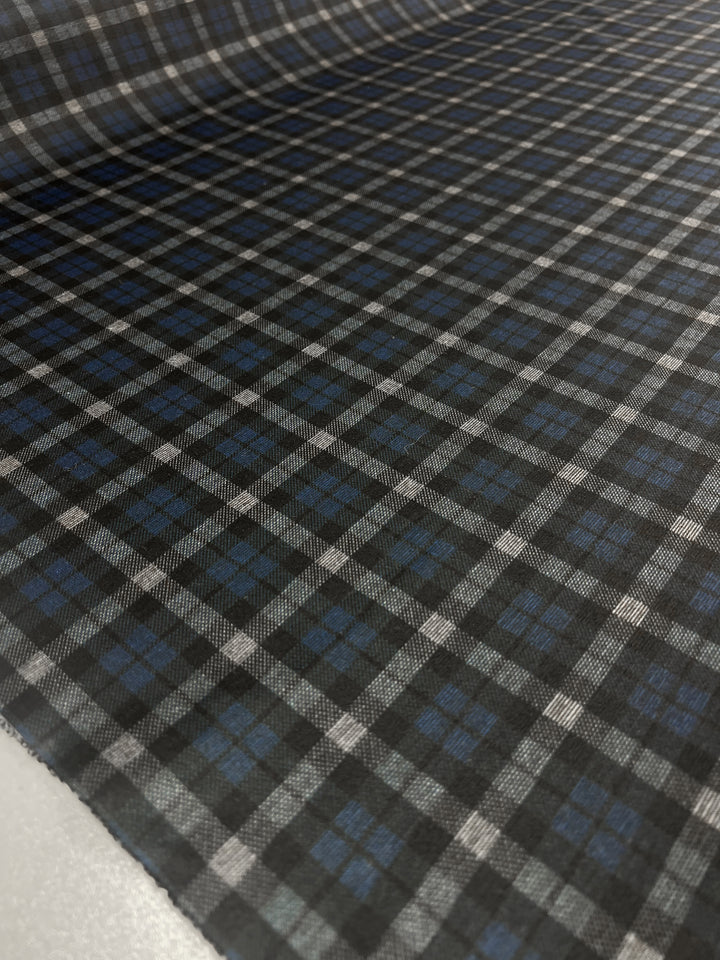 A close-up view of the medium-weight Ponte - Checkers fabric from Super Cheap Fabrics, showcasing its intricate plaid pattern. The design features intersecting lines and squares in shades of black, gray, white, and blue. The polyester material appears to be spread out on a flat surface, making it ideal for crafting stylish pants.