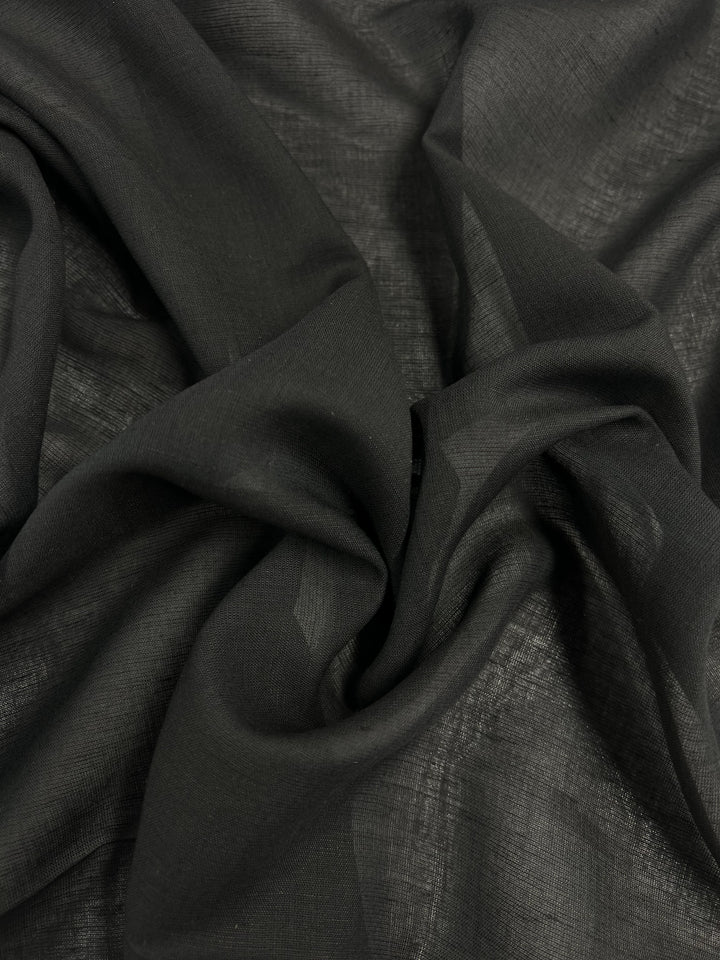 Close-up of a piece of dark, crumpled fabric, likely black in color. The Linen Voile - Bristol Black from Super Cheap Fabrics appears to be semi-sheer with a slight texture visible across its surface. The material forms gentle folds and gathers.