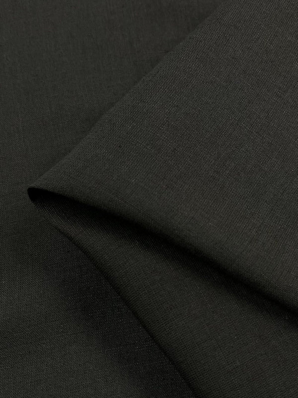 A close-up image reveals the texture of a piece of Linen Voile - Bristol Black - 146cm from Super Cheap Fabrics. The fabric has a smooth and slightly matte surface, with part of it folded over creating a subtle shadow.