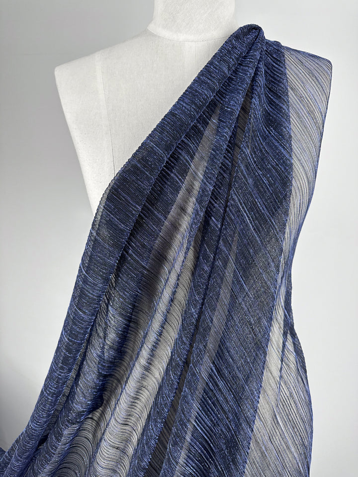 A mannequin adorned with the Metallix Pleat - Cobalt Metal fabric from Super Cheap Fabrics, highlighting its texture and flow. The sheer navy blue polyester material gracefully drapes over the upper half of the mannequin, offering a stylish and sophisticated appearance.