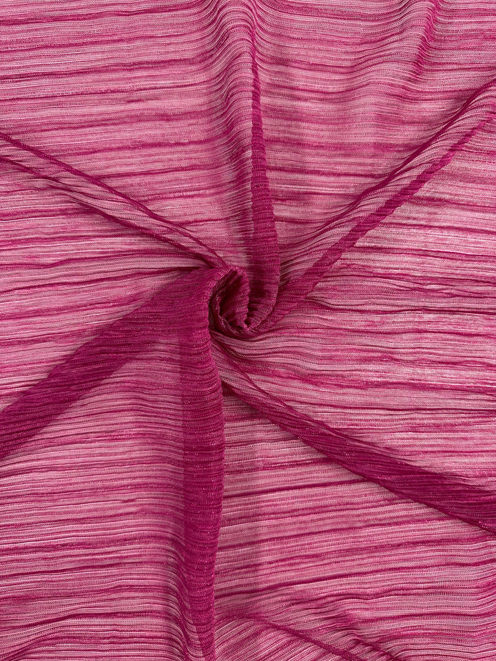 A close-up of the Metallix Pleat - Hot Pink - 140cm fabric from Super Cheap Fabrics showcases its pink, sheer polyester design with horizontal stripes, artfully gathered in the center to create a spiral pattern. The metallic hot pink finish adds a subtle shimmer that enhances the textured appearance of this lightweight fabric.