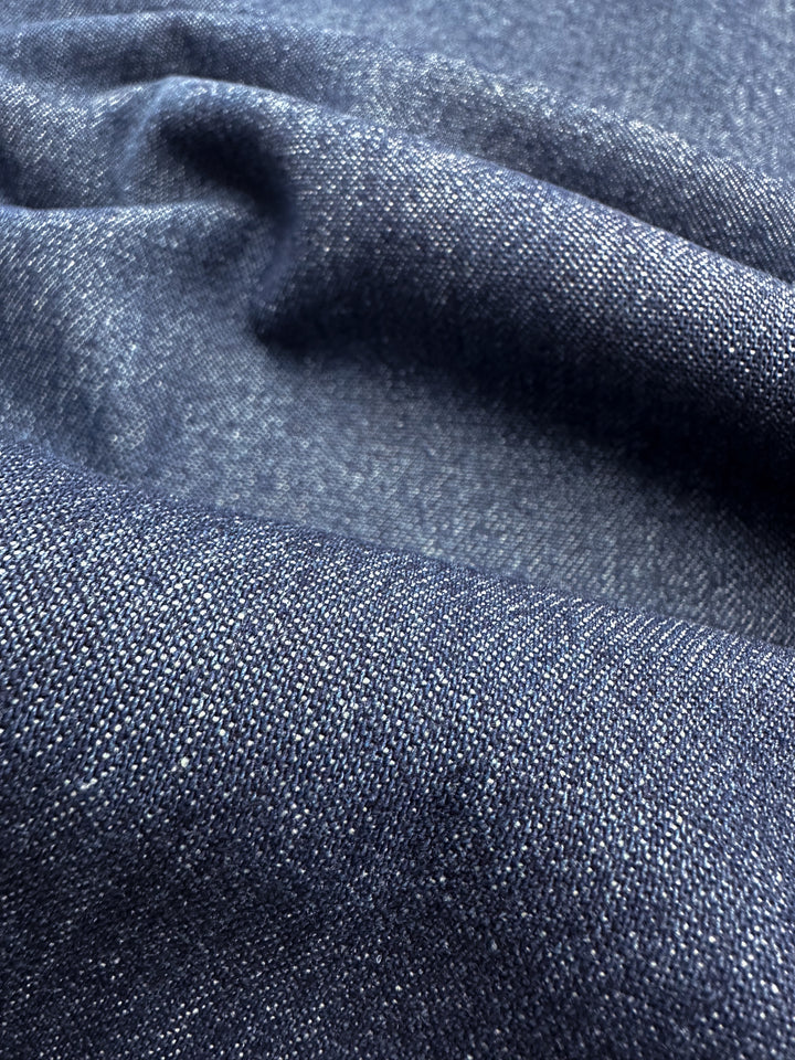 A close-up of the Denim - Oceana - 150cm fabric from Super Cheap Fabrics reveals its dark blue texture with visible folds and a woven pattern. Made from 100% cotton, it displays subtle color variations that emphasize the material's quality.