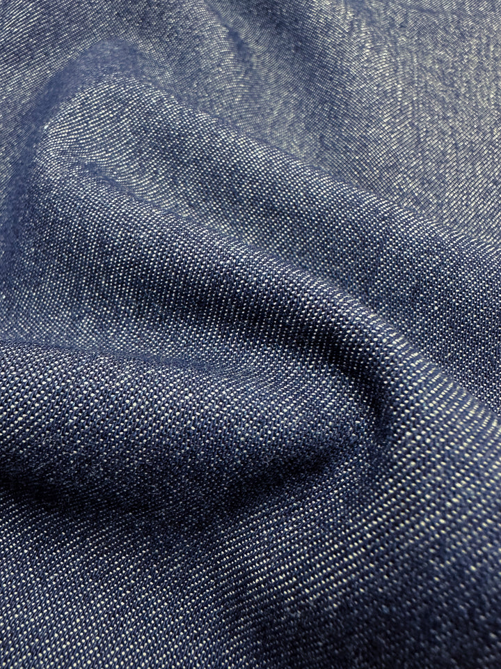 Close-up of Super Cheap Fabrics' "Denim - Outer Space - 150cm," featuring a dark blue shade crafted from premium cotton ring-spun yarns. The visible weave texture highlights the material's slight creasing, demonstrating its thickness and remarkable durability.