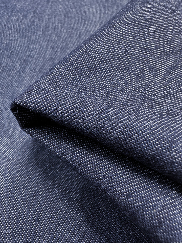 Close-up of the Outer Space dark blue denim fabric, crafted by Super Cheap Fabrics, featuring a visible woven texture with a slight fold. This material, made from ring-spun yarns, displays the distinctive diagonal pattern typical of denim, with highlights and shadows that showcase its thickness and grain. The fabric measures 150cm in width.